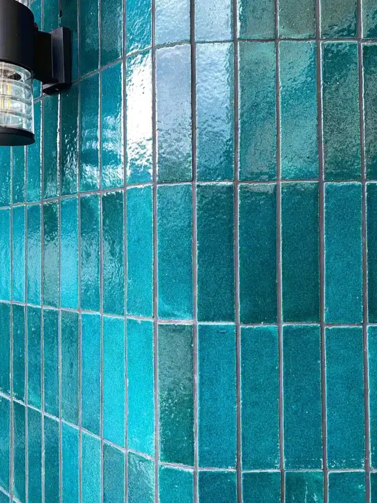 Carreaux de Céramique Turquoise : Design et Éclat Mural Carreaux de céramique turquoise brillant en pose verticale avec luminaire noir, texture artisanale et reflets.