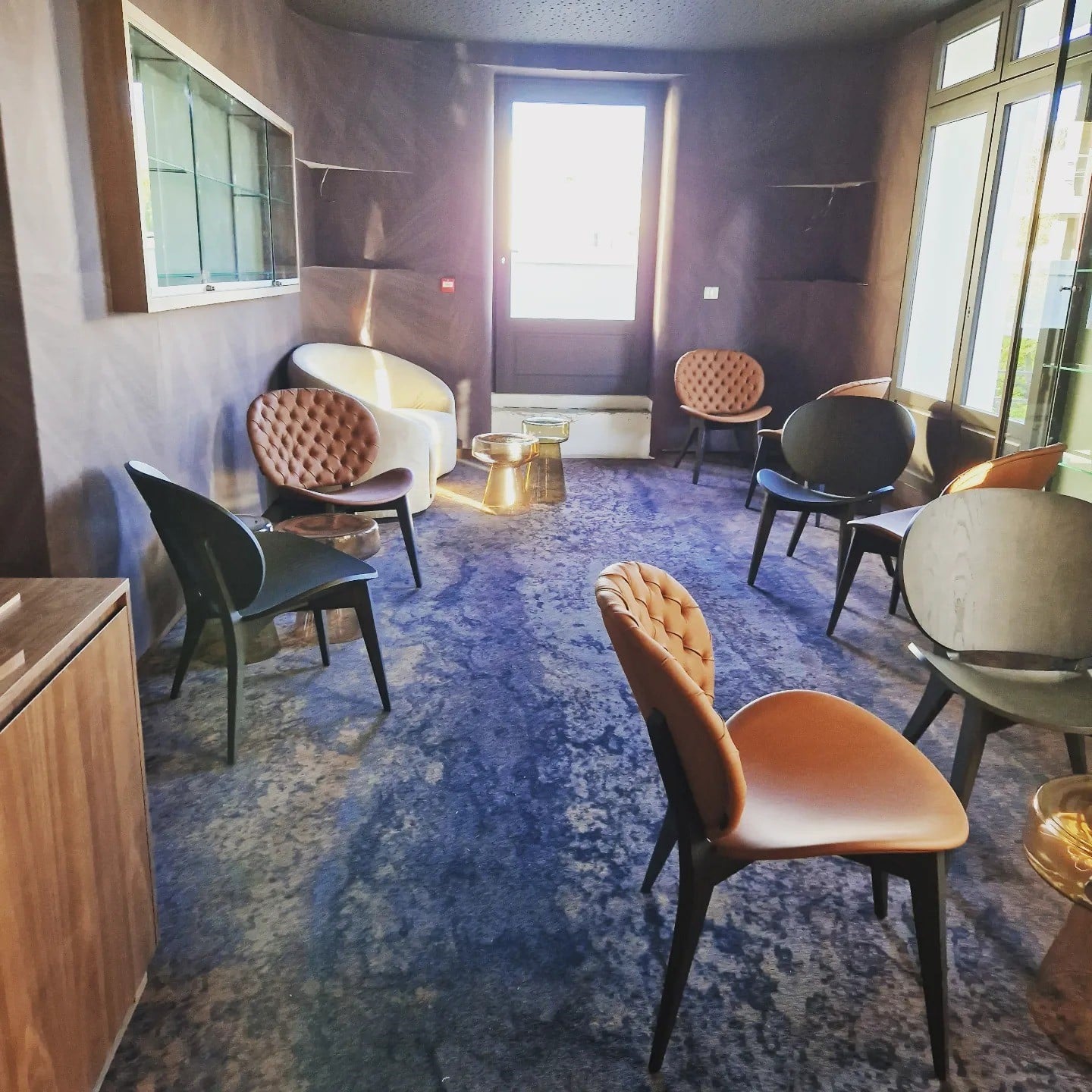 Salon chic avec fauteuils capitonnés marron, chaises noires et tapis bleu. Design intérieur moderne et lumineux.