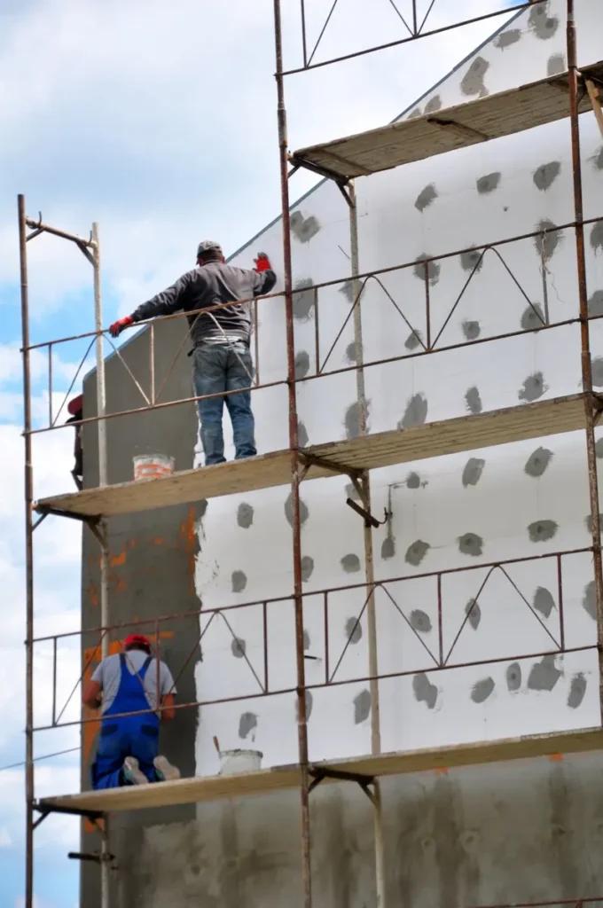 Isolation thermique extérieure : ouvriers sur échafaudage Deux ouvriers sur un échafaudage réalisent l'isolation thermique par l'extérieur d'une façade de bâtiment.