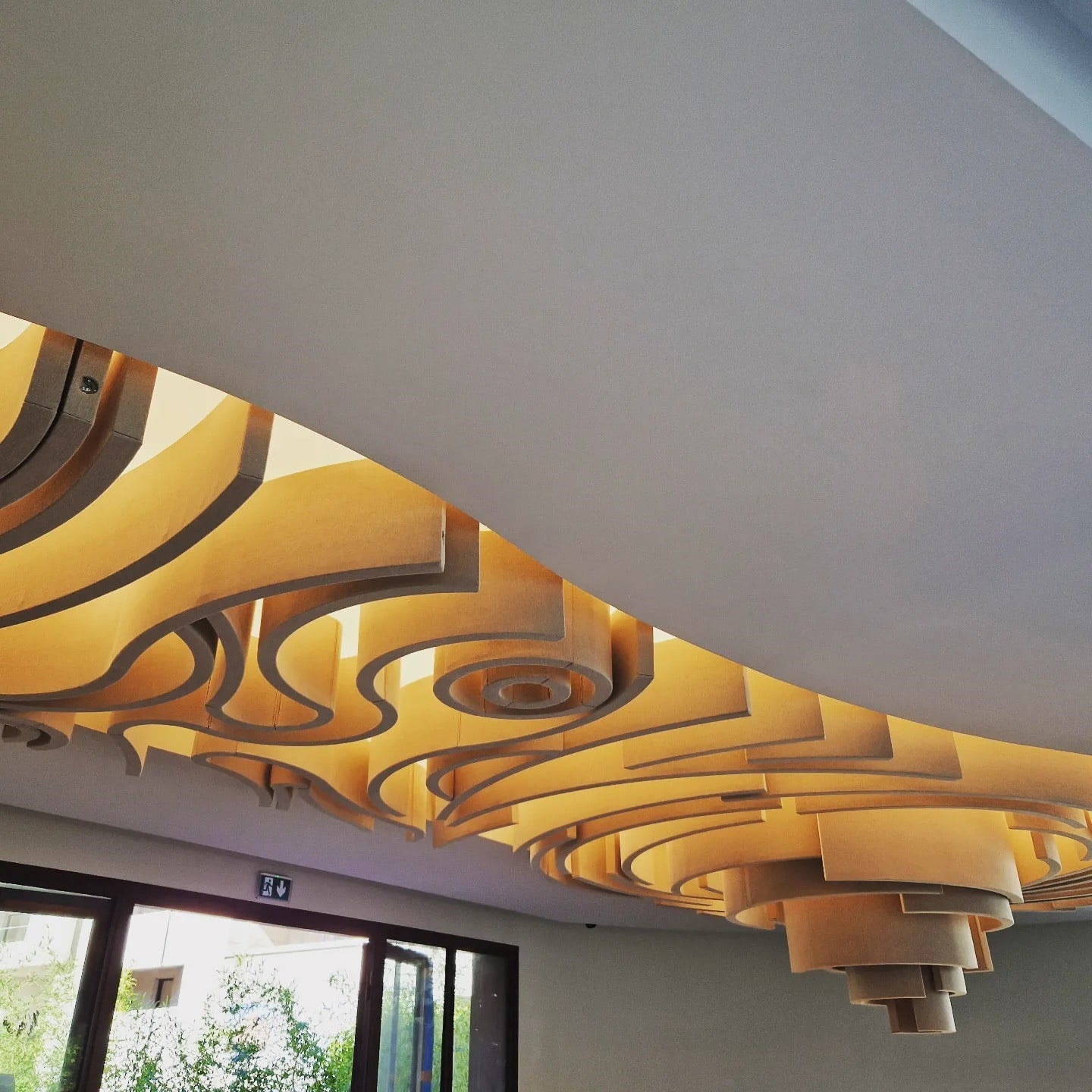 Plafond artistique aux panneaux ondulés rétroéclairés d'une lumière dorée chaude, design intérieur moderne et organique.