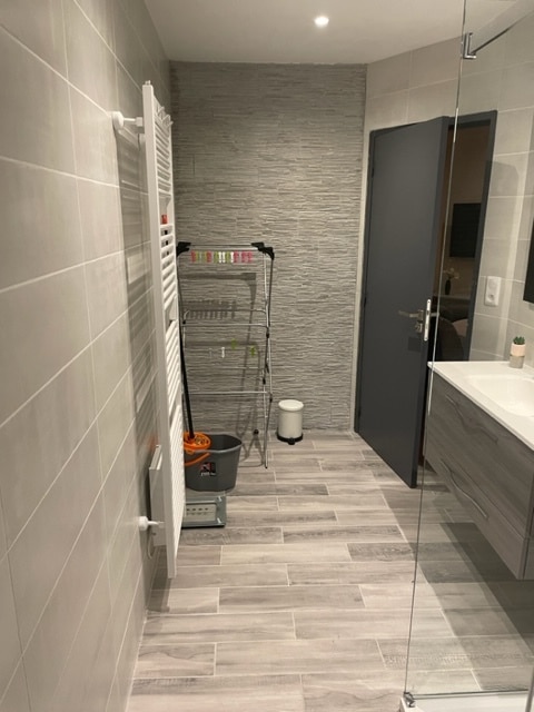 Salle de bain moderne avec carrelage gris, mur texturé, sèche-serviettes blanc et meuble vasque suspendu.